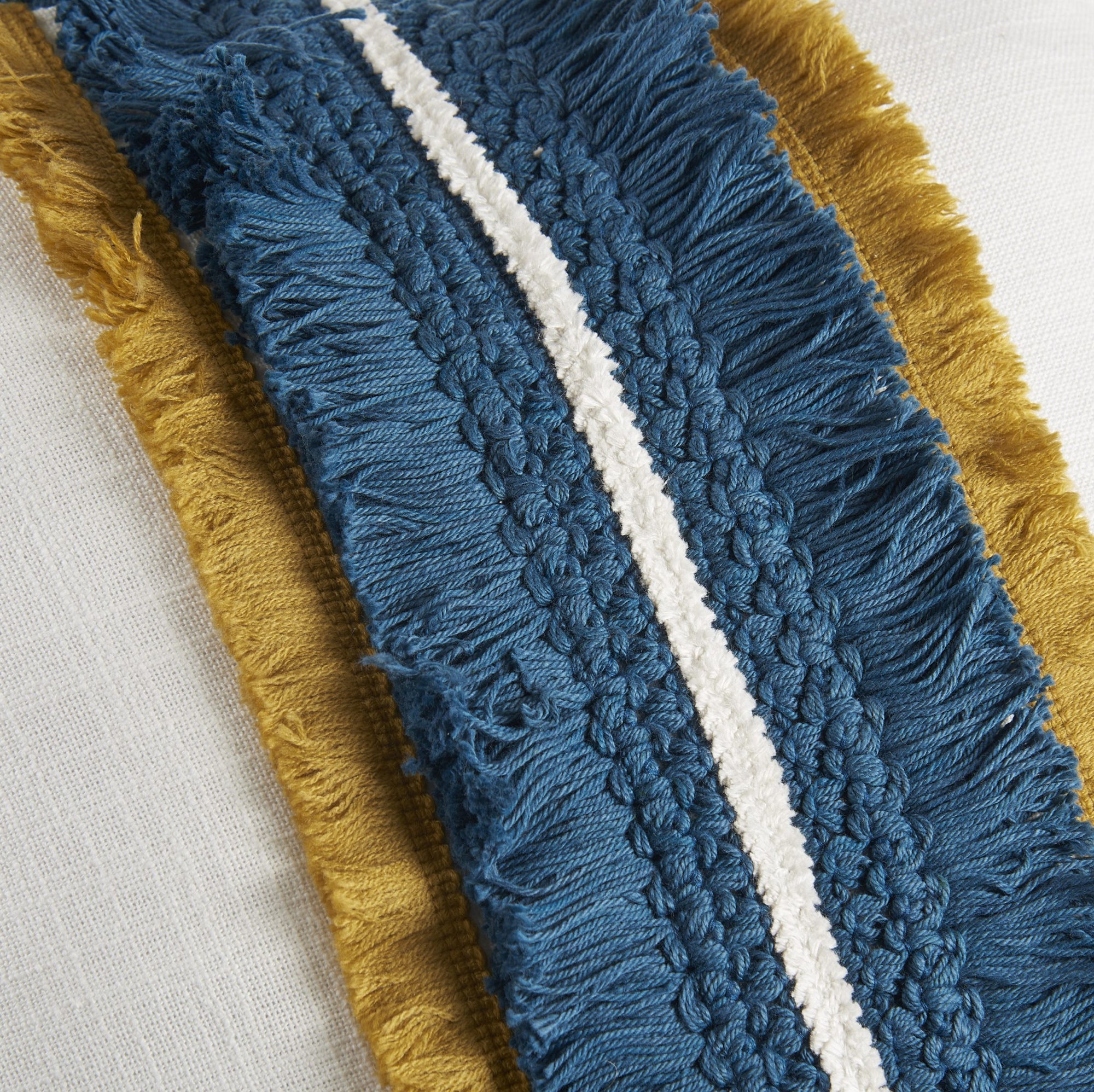 Cuscino quadrato bianco con frange blu e ocra. L'oca nera